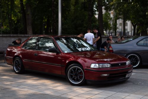 Free A classic red Honda Accord parked on a paved street with people in the background. Stock Photo
