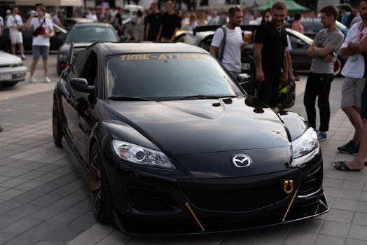 Black Mazda RX-8 showcased at a car event, surrounded by an audience on a sunny day.