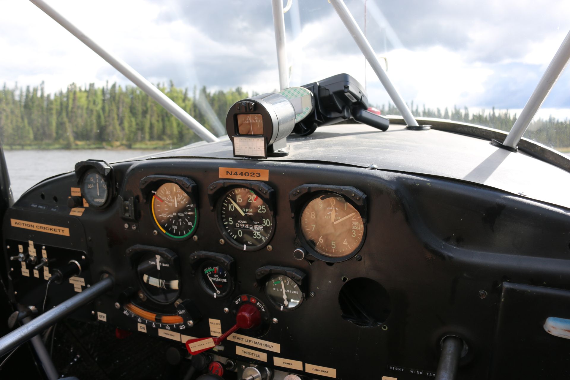 Close-up of a vintage airplane cockpit with analog gauges and scenic forest view outside.