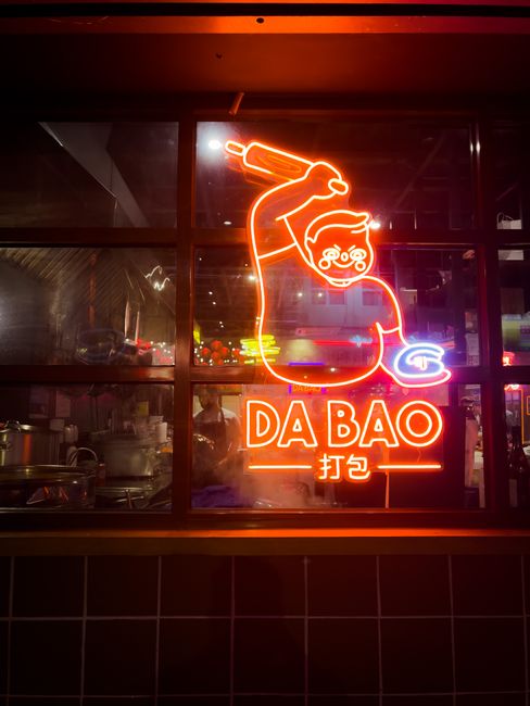 100g Hạt Macca Chứa Bao Nhiêu Calo? Ăn Có Gây Béo Không? 3 Glowing neon DA BAO sign illuminates a restaurant window at night, creating a vibrant urban scene.