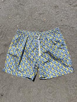 Vibrant blue and yellow patterned shorts displayed against sandy backdrop under bright sunlight.