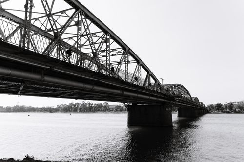 Free Monochrome image of a classic steel bridge spanning a calm river, emphasizing its architectural elegance. Stock Photo