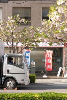 Street view of a truck passing by blooming cherry blossoms and city buildings, capturing spring in an urban setting.