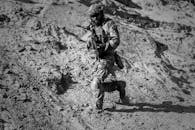 一名士兵全副战斗装备，在严酷的沙漠阳光下跑下沙丘