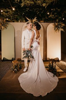 A sophisticated couple in wedding attire sharing a moment indoors under decorative lights.