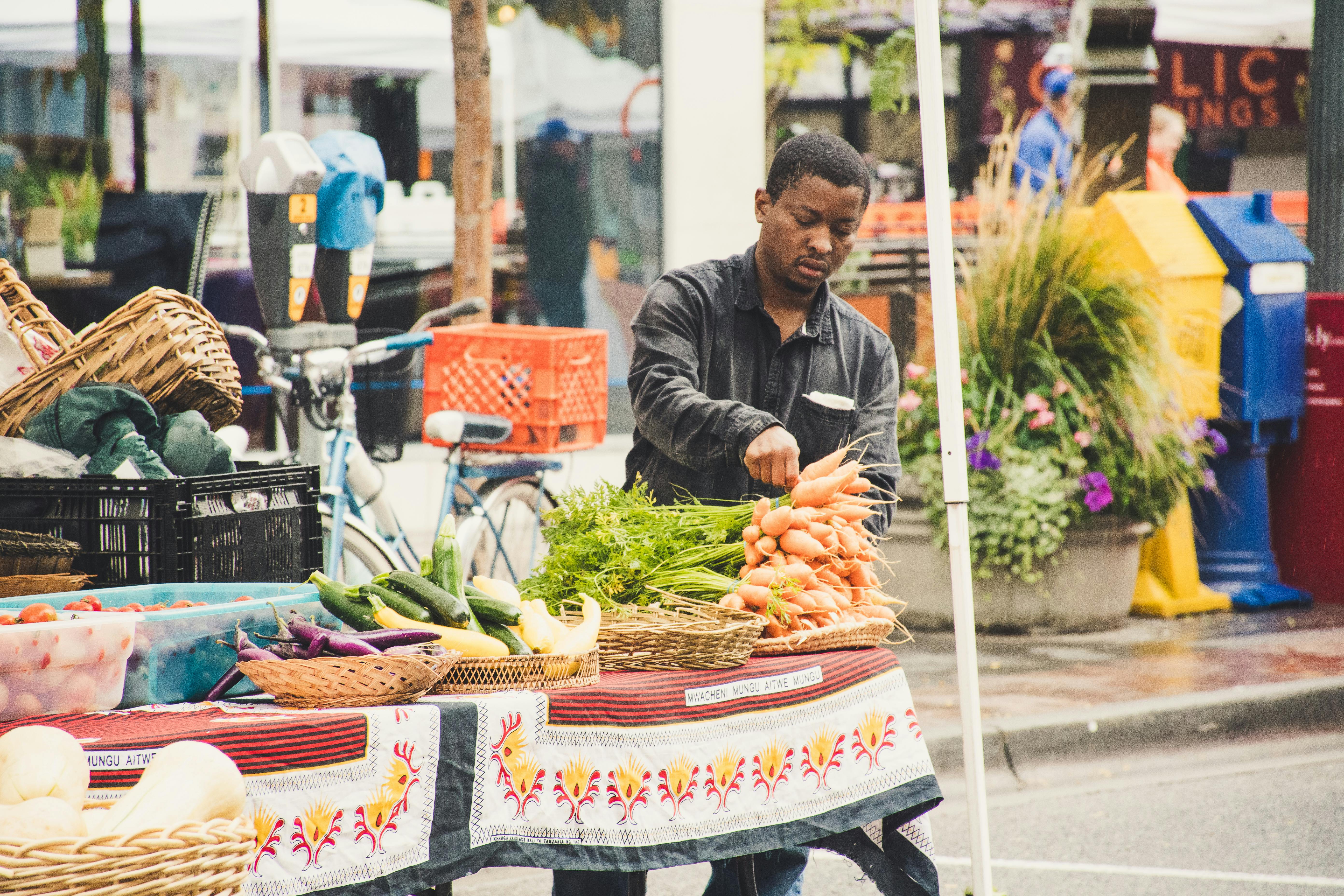 man standing beside table with vegetables near buildings