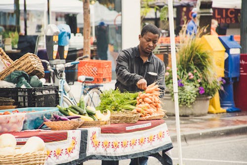 Man Standing Beside Table With Vegetables Near Buildings