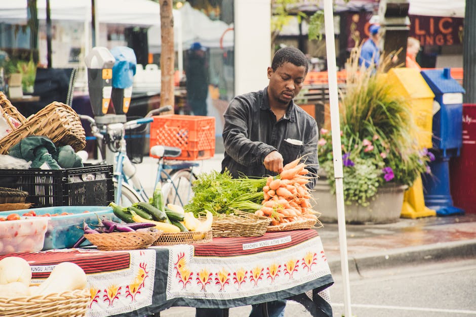 Man Standing Beside Table With Vegetables Near Buildings