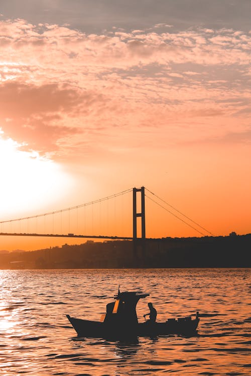 Silhouetted Boat in the Water and Bridge in the Background at Sunset 