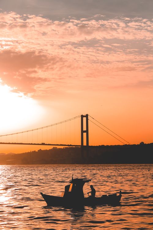 Free Silhouette of a boat in front of a bridge during a stunning summer sunset. Stock Photo