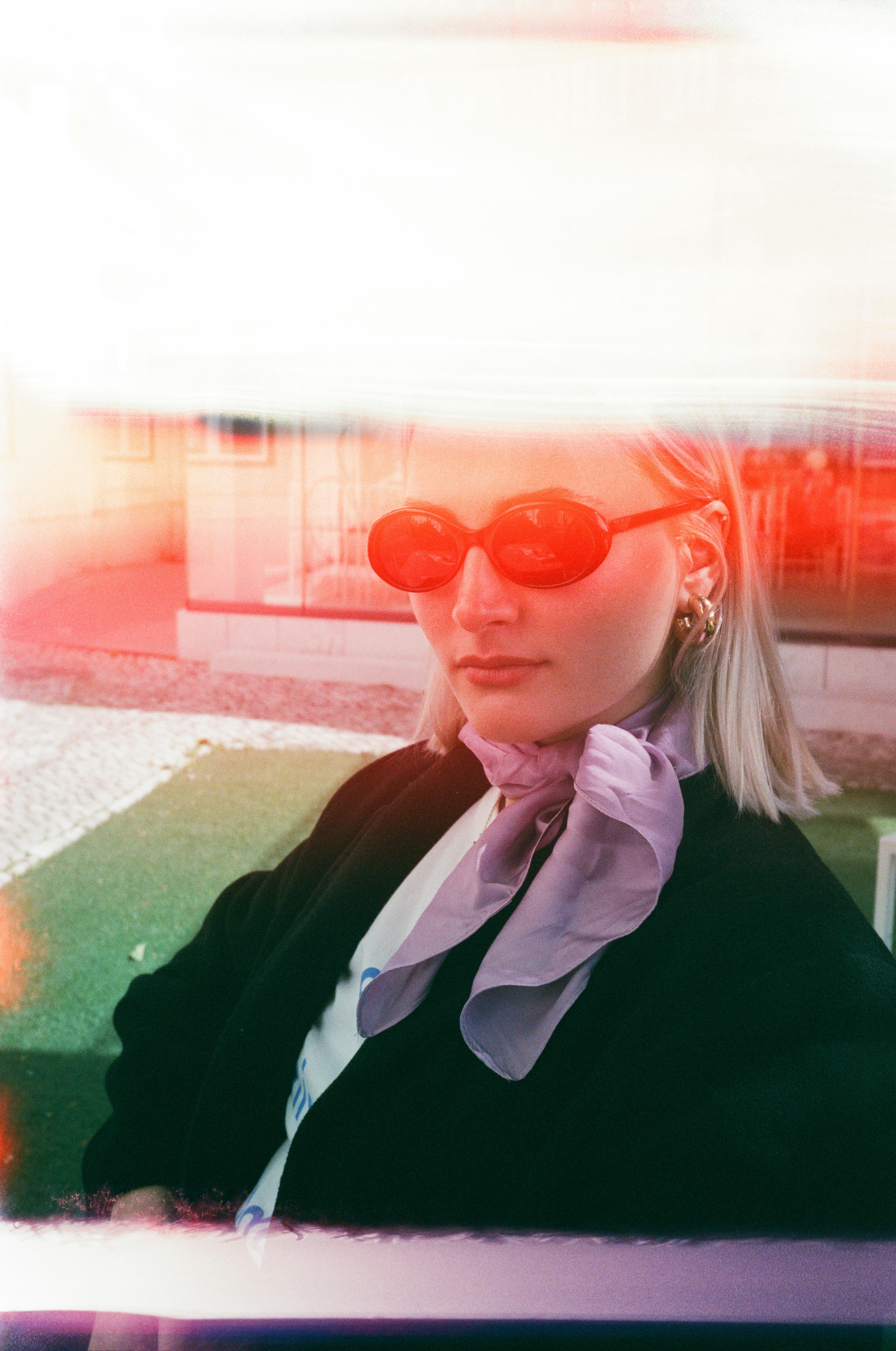 Portrait of a fashionable woman wearing sunglasses and a scarf, captured in an artistic outdoor setting.