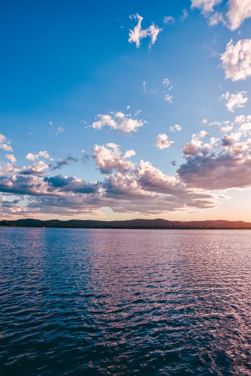 A sunset over a lake with clouds in the sky · Free Stock Photo