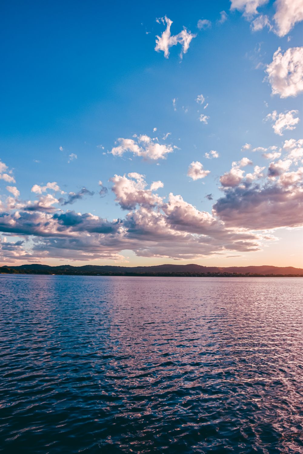A sunset over a lake with clouds in the sky · Free Stock Photo
