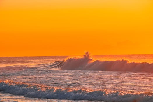 A stunning sunset over the ocean with waves crashing, creating a serene and vibrant seascape.