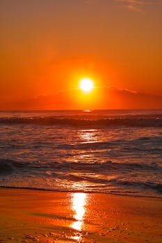 A tranquil sunset over the ocean with vibrant orange hues reflecting on the water.