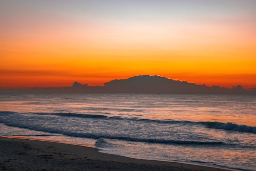 Capture of a serene ocean sunrise with vibrant orange hues reflecting on the water.