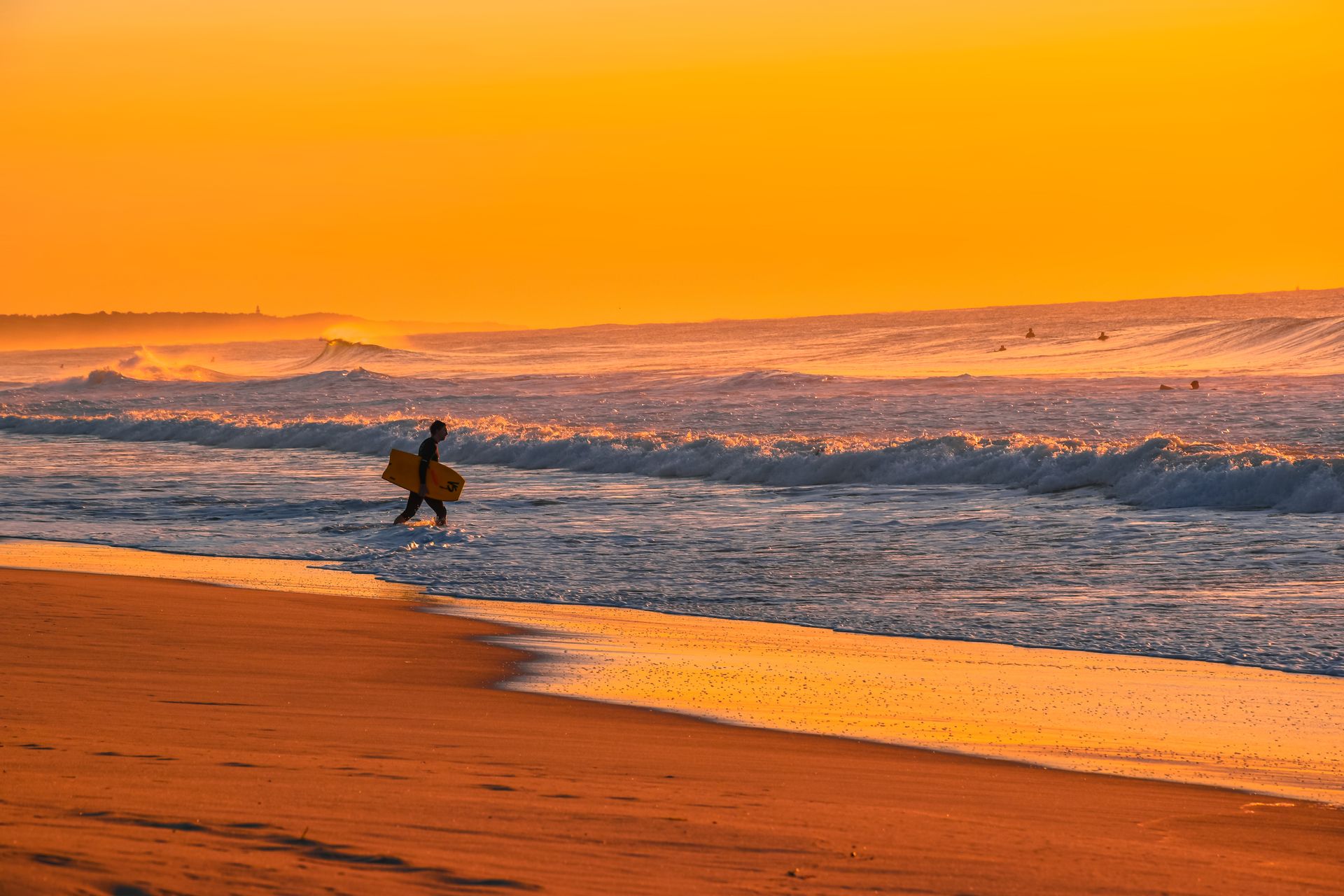 Surfer walking along the beach at golden sunset