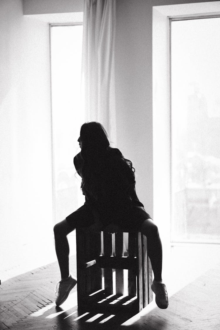 Woman Sitting On Box In Room In Black And White