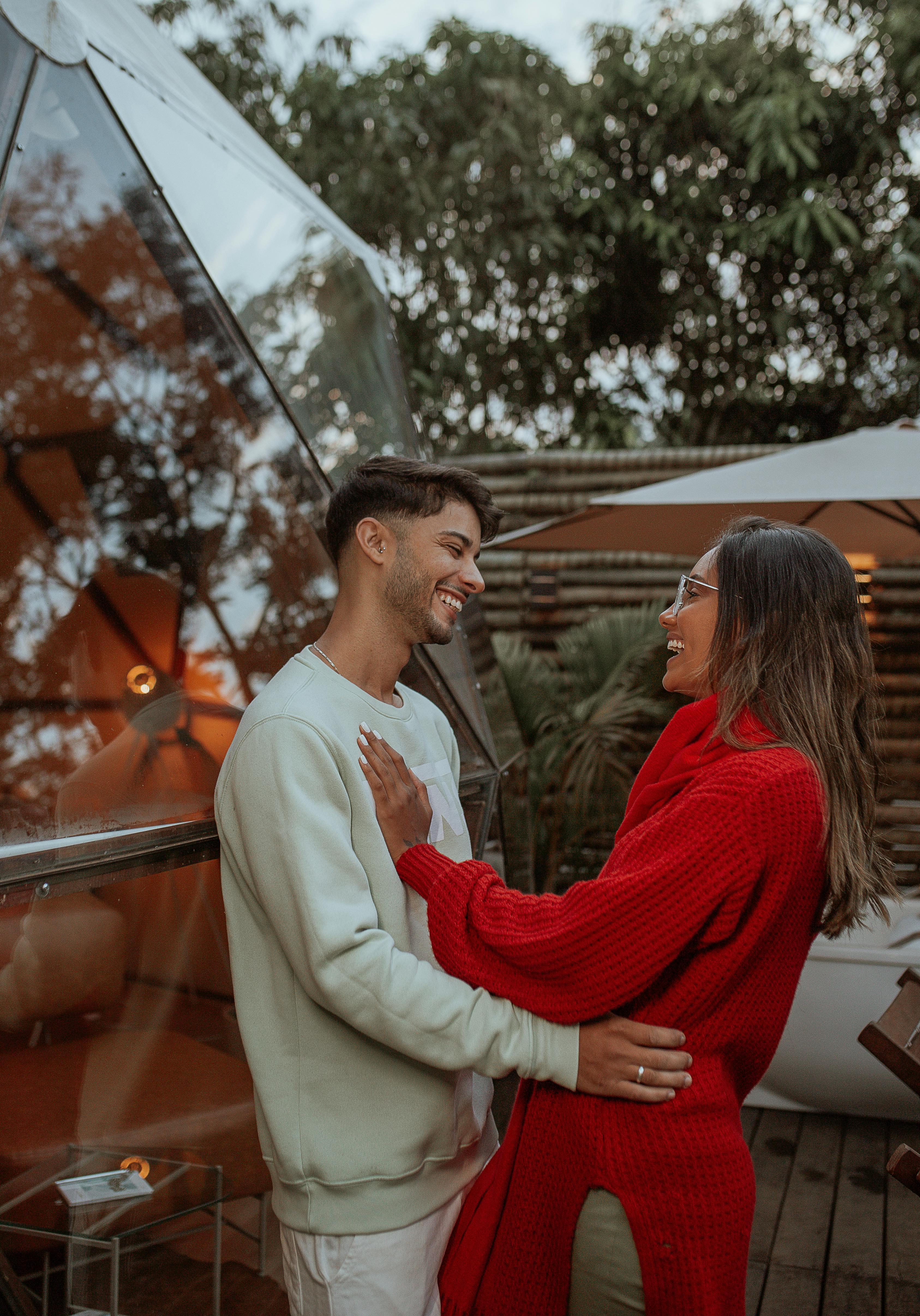 A joyful couple embraces outdoors, showcasing modern fashion style surrounded by nature.