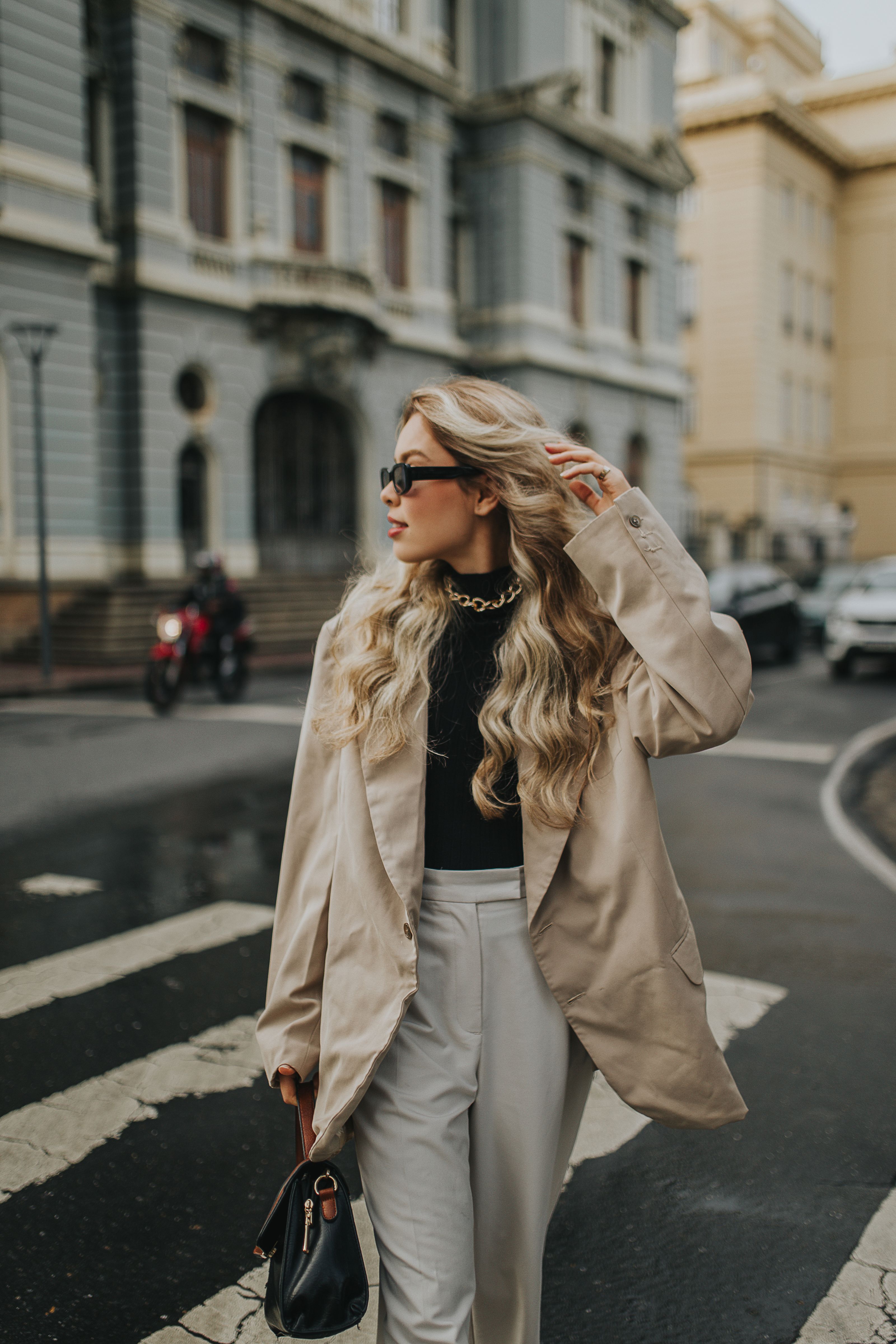 Uma mulher fashion caminhando em uma rua da cidade usando óculos de sol e um traje estiloso.