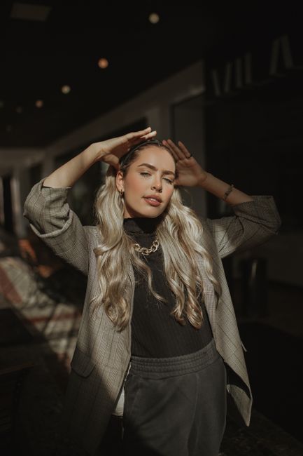 Elegant portrait of a fashionable woman with long blonde hair posing indoors with dramatic sunlight.