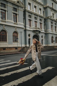 Stylish woman holding a bouquet crosses a city street in front of a historical building.