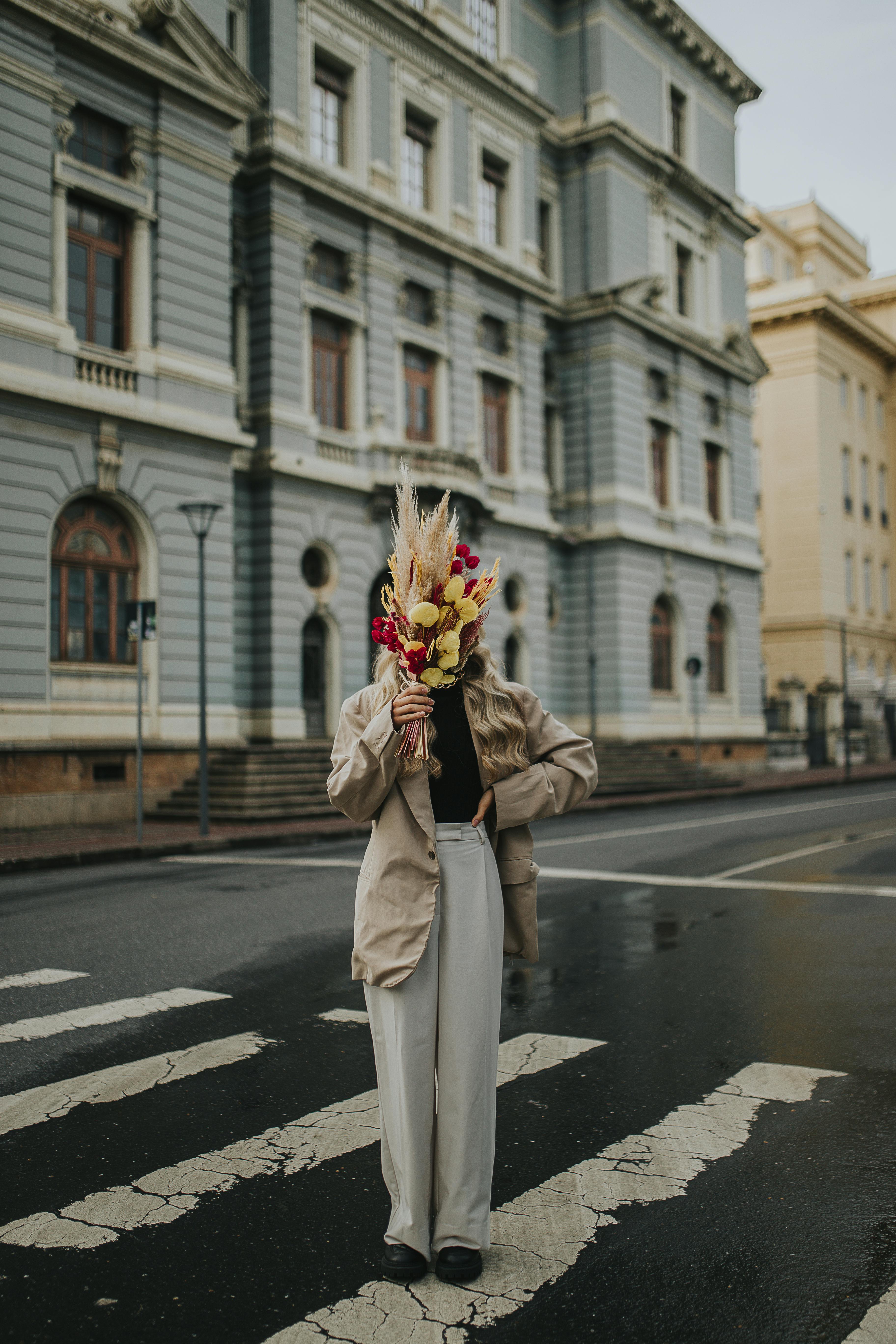 Woman in street holding flowers, blending urban style with nature.
