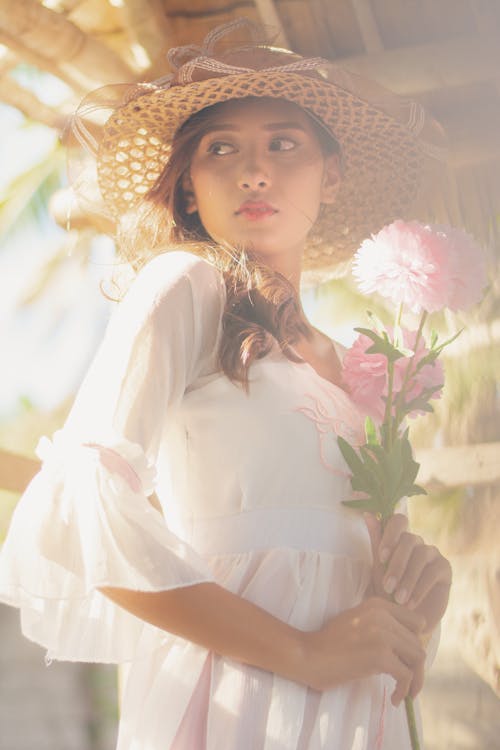 Young Woman in a White Dress and a Hat Holding Flowers