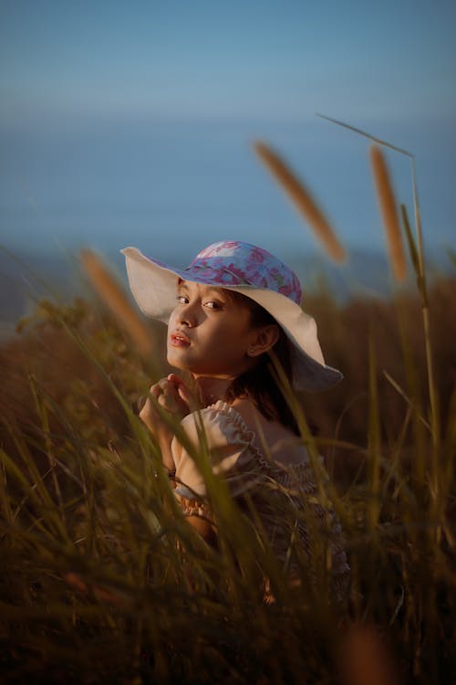 Young Woman in a Hat Sitting on a Grass Field 
