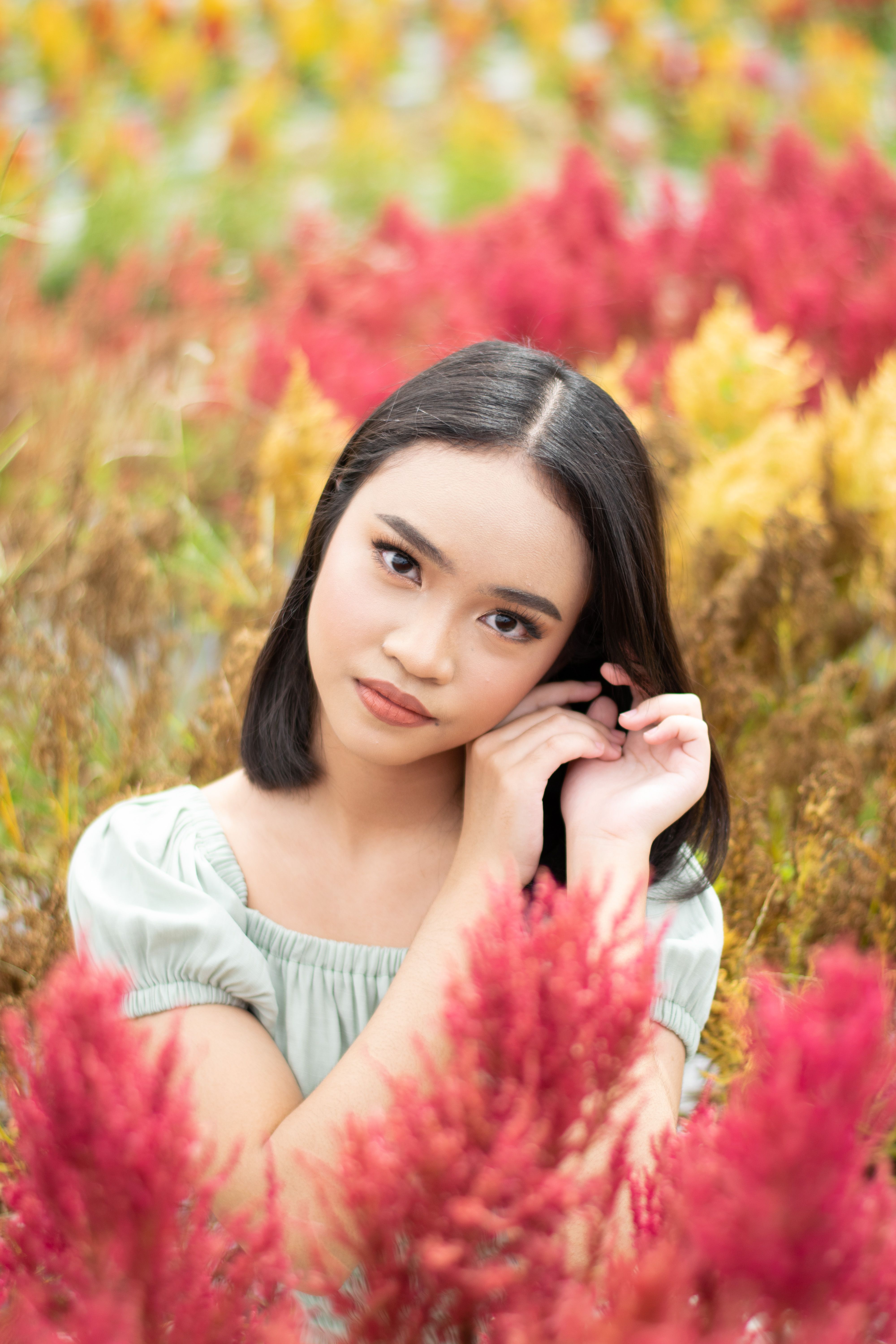 A young woman poses gracefully in a vibrant field of red and yellow flowers.