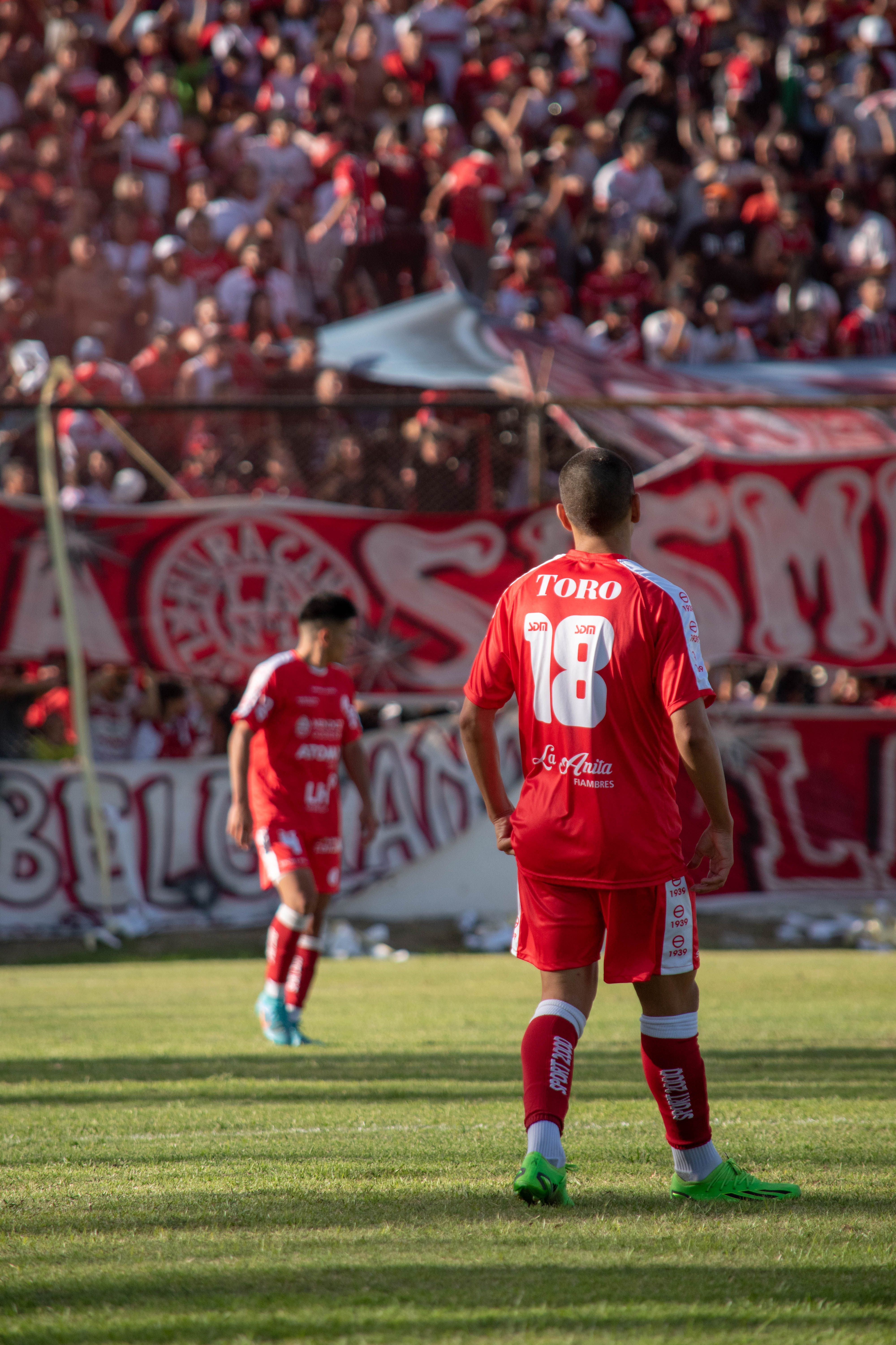 Soccer players in red uniforms on field during an exciting match with a cheering crowd.