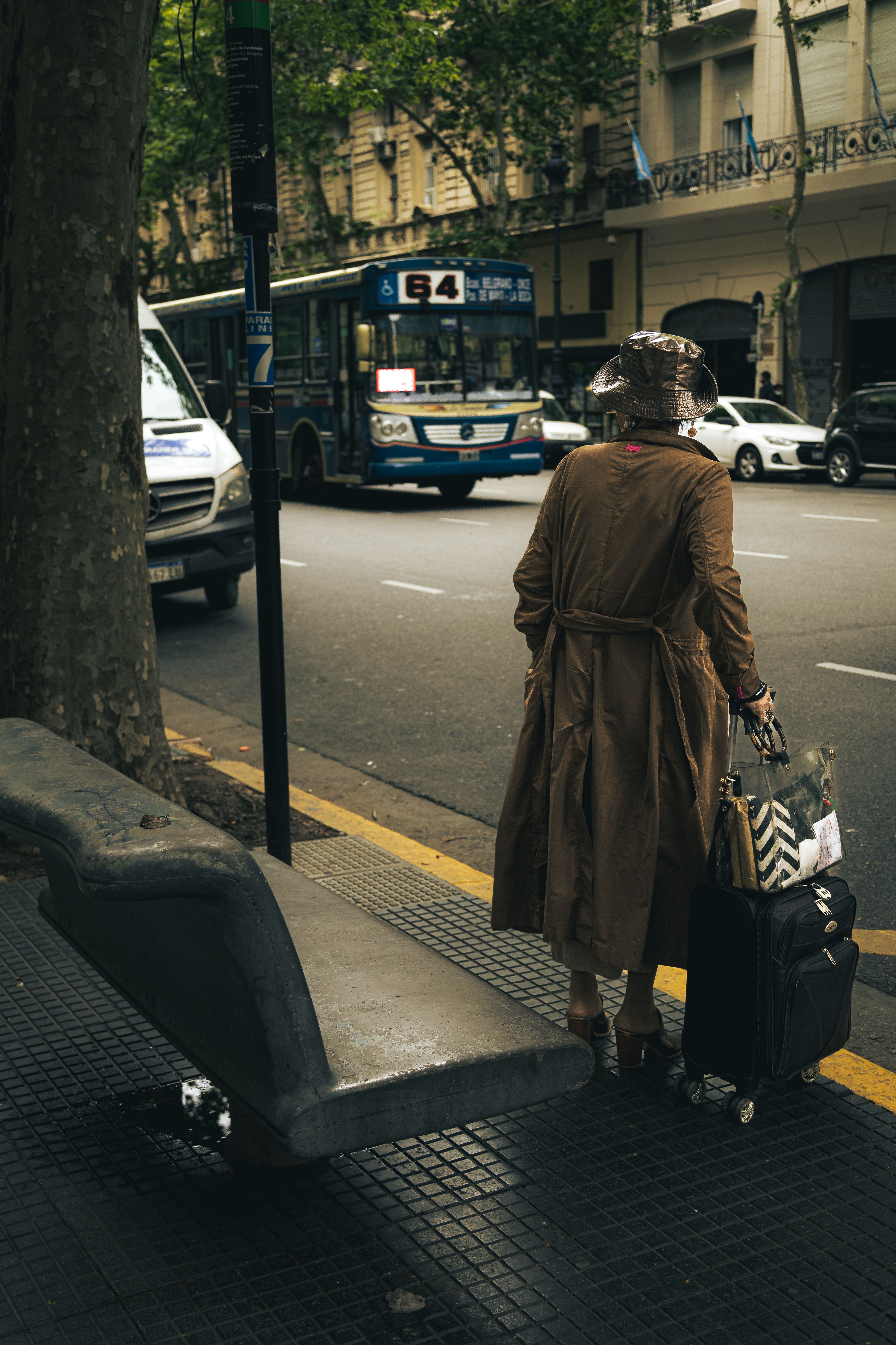 A woman in coat stands with luggage on a bustling street in Buenos Aires, Argentina.