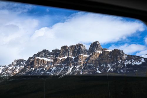 Free Snow-capped Castle Mountain peaks framed by car window under a blue sky. Stock Photo