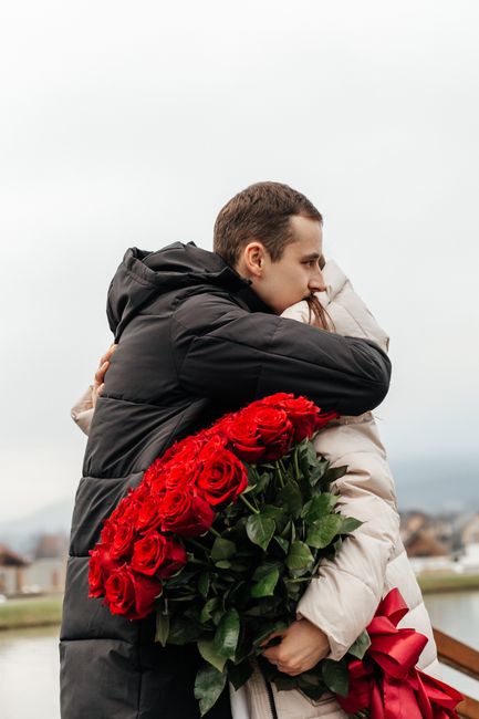 A couple embraces outdoors with a bouquet of red roses, symbolizing love.