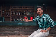 一个穿着条纹衬衫的年轻人坐在时尚的酒吧里喝着鸡尾酒