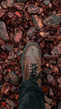 Close-up image of a brown boot standing on rugged, wet, reddish rock surface.