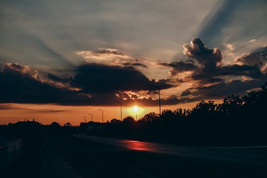 Dynamic sunset view over a quiet road in Pécel, Hungary, capturing vibrant clouds and silhouette of trees.