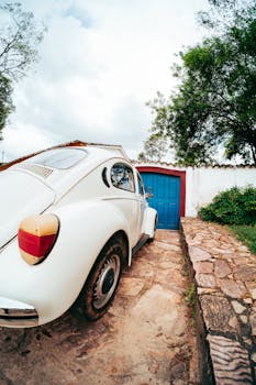 Retro white car on cobblestone driveway in Tiradentes, Brazil showcased against a blue door.