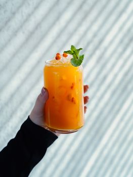 Close-up of a refreshing orange juice with ice and mint in a glass, held by a hand.