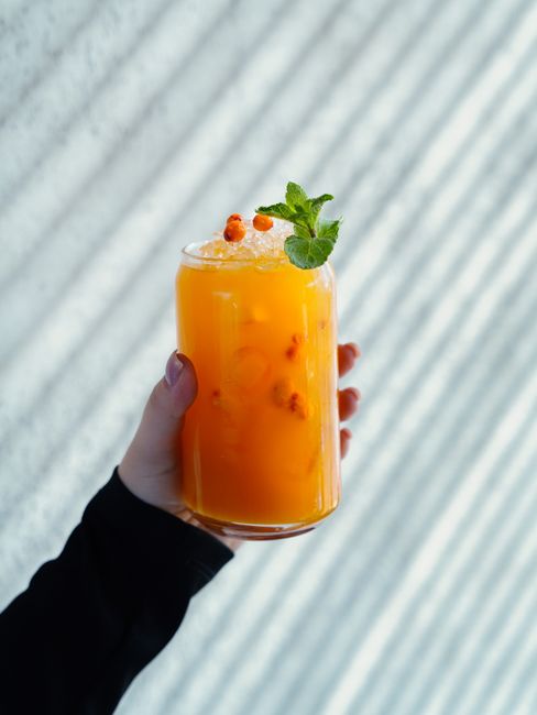 Close-up of a refreshing orange juice with ice and mint in a glass, held by a hand.