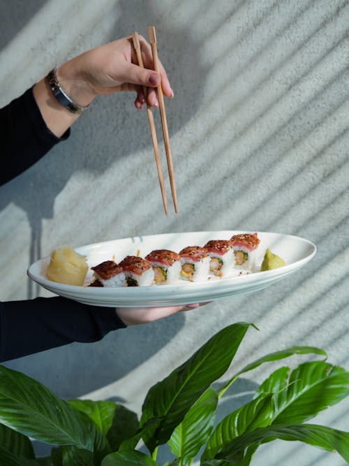 Close-up of Woman Holding a Plate with Sushi and Chopsticks