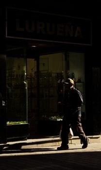Silhouetted man walks past a shop in the city, casting strong shadows.