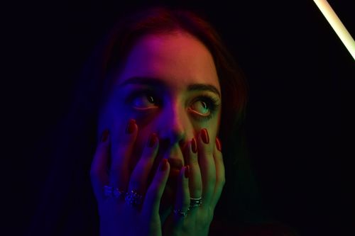 Free A close-up portrait of a woman with colorful lighting, hands on face, in dark background. Stock Photo