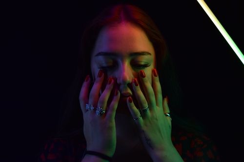 Free Close-up portrait of a woman with colorful neon lights and closed eyes, showcasing rings and red nails. Stock Photo
