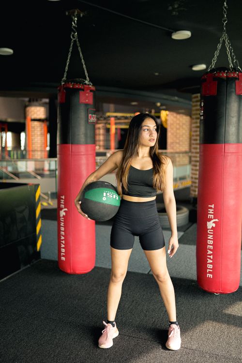 Free Woman standing in a gym holding a medicine ball, ready for exercise. Fit lifestyle focus. Stock Photo