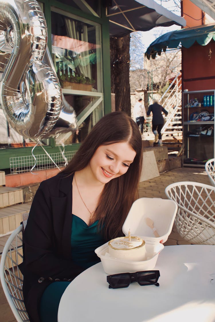 Young Woman Sitting At The Table With A Birthday Cake And Balloons 