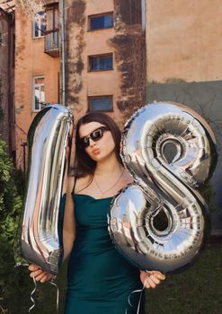 Young woman celebrating her 18th birthday outdoors with large balloons in an urban setting.