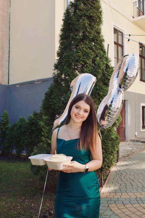 Young Woman in a Dress Holding Balloons with the Number 18 and a Birthday Cake 