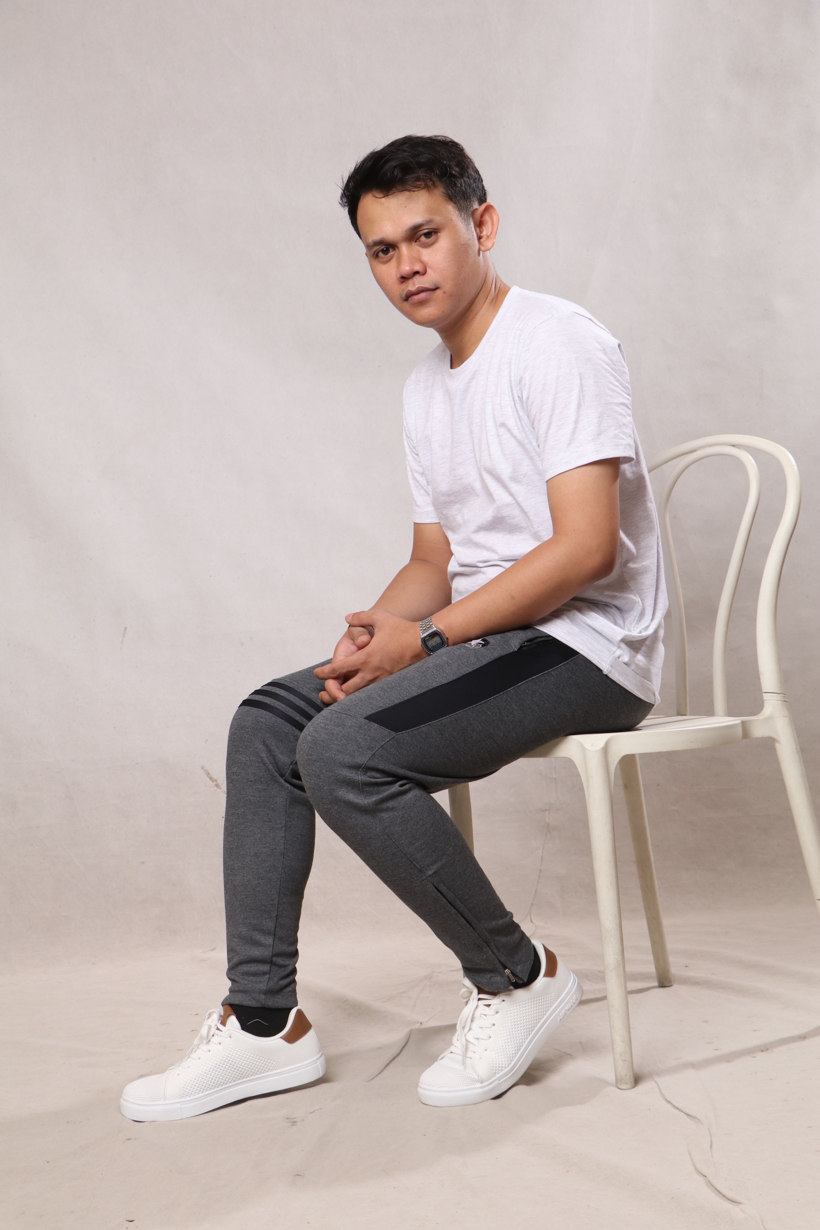 Young man in casual attire posing on a chair in a studio setting.