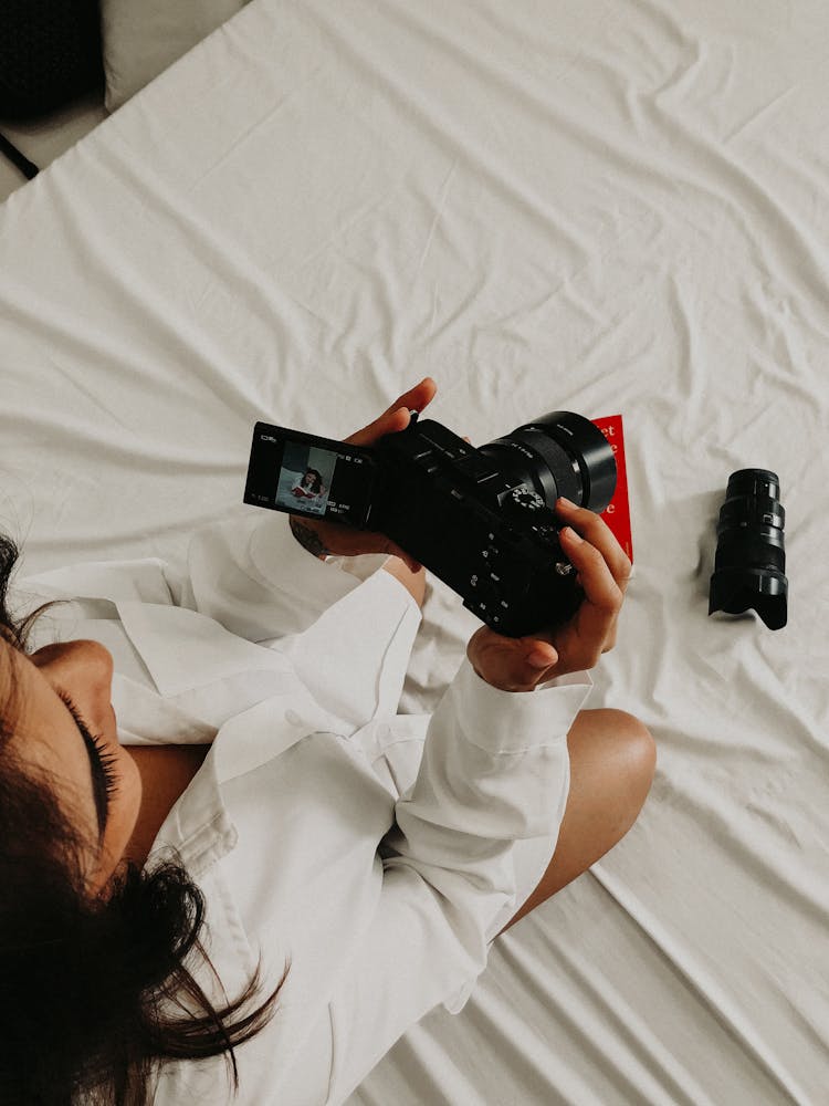 Woman In White Shirt Sitting With Camera On Bed